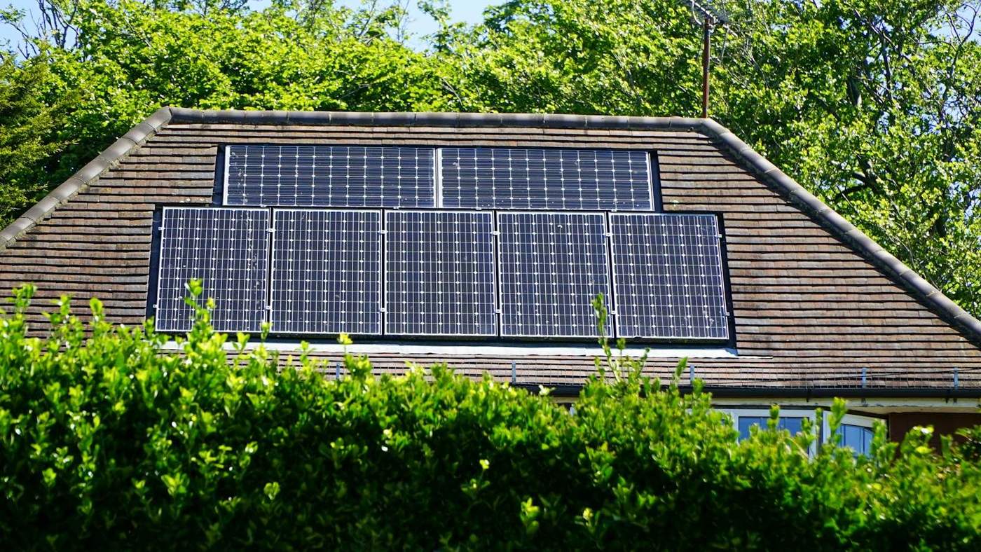 Zonnepanelen op een pannendak achter een haag